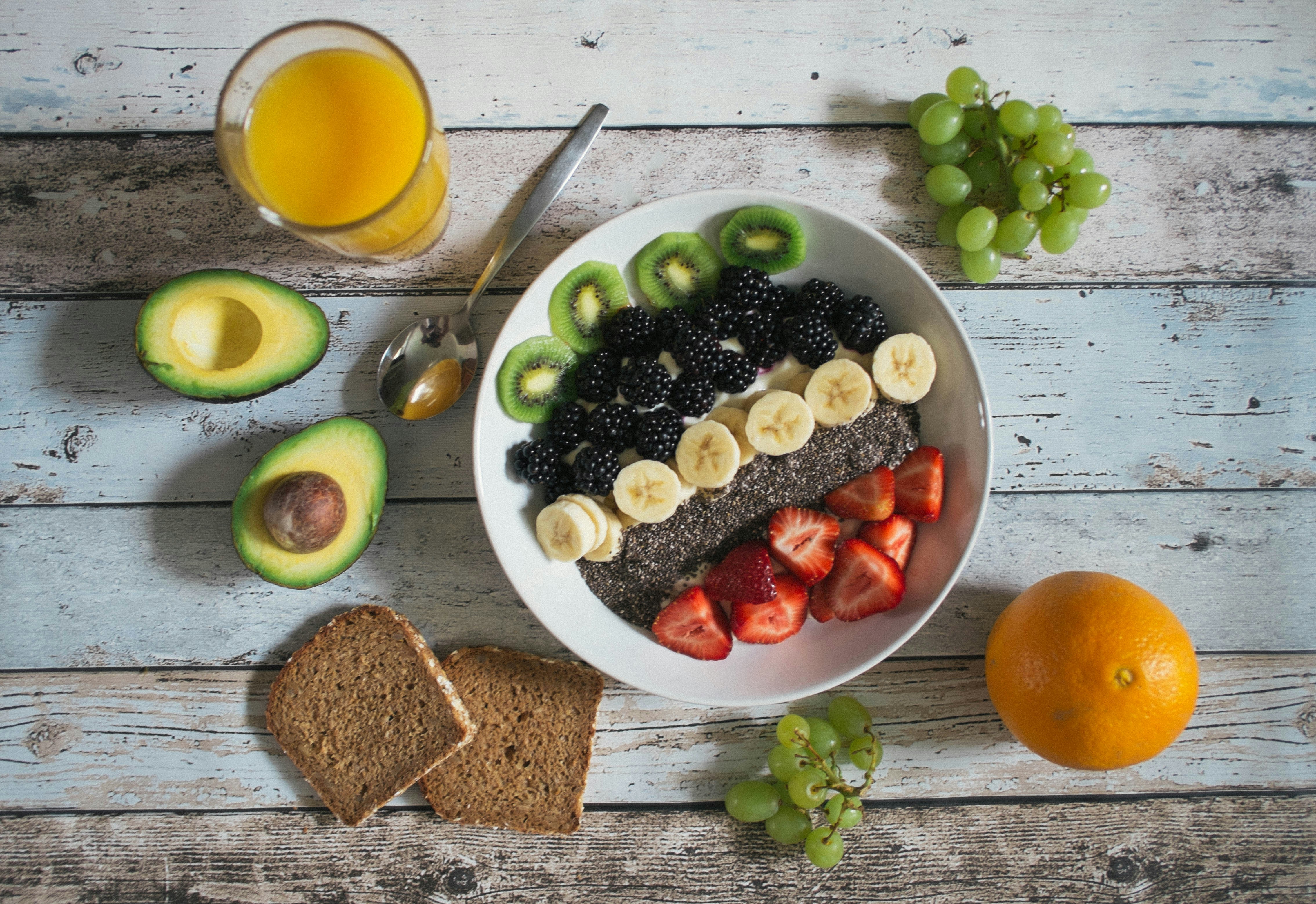 Bovenaanzicht van een gezond ontbijt met fruit, avocado, brood en vers sinaasappelsap op een rustiek houten tafelblad