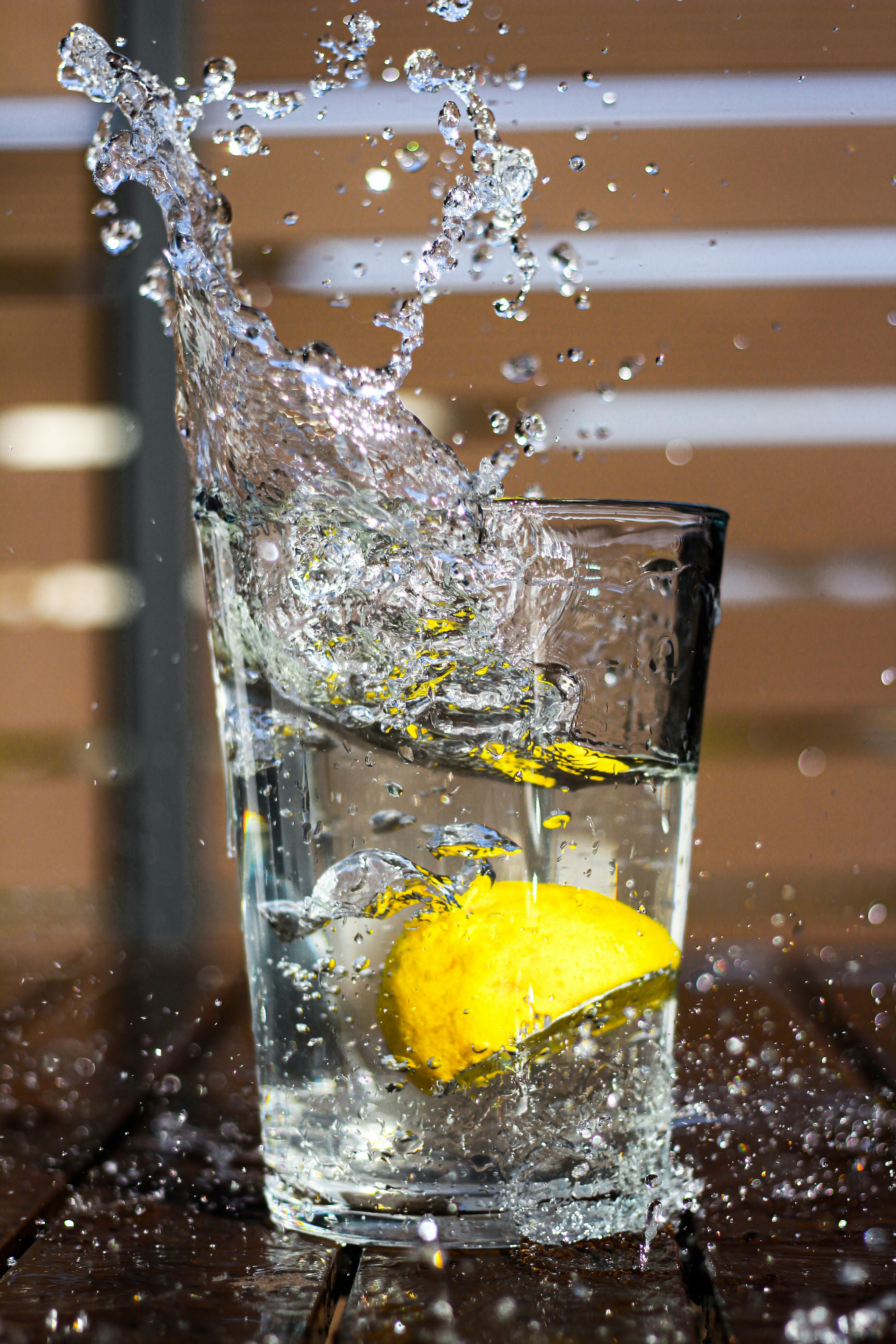 Een schijfje citroen dat in een glas helder water valt, met opspattende waterdruppels